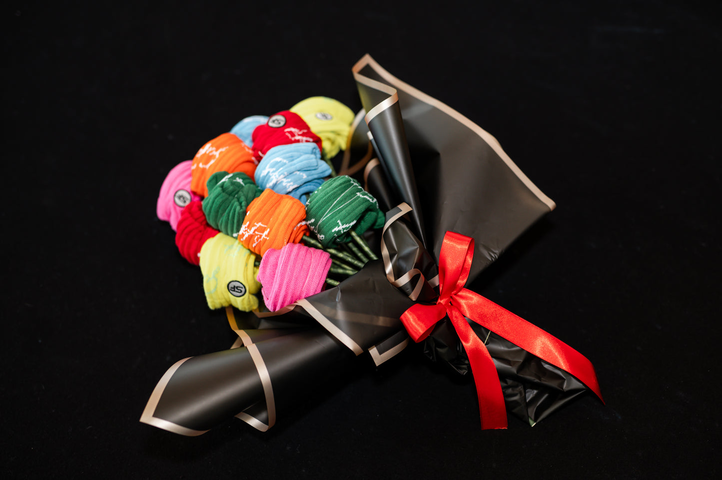A bouquet of multicolored crew compression socks with a red ribbon, arranged in a manner resembling a traditional flower bouquet, on a black background.