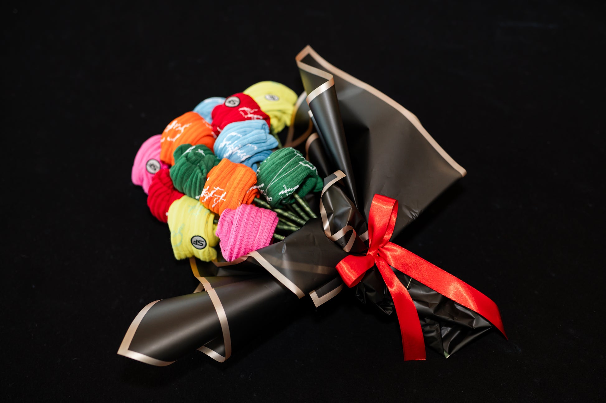 A bouquet of multicolored crew compression socks with a red ribbon, arranged in a manner resembling a traditional flower bouquet, on a black background.