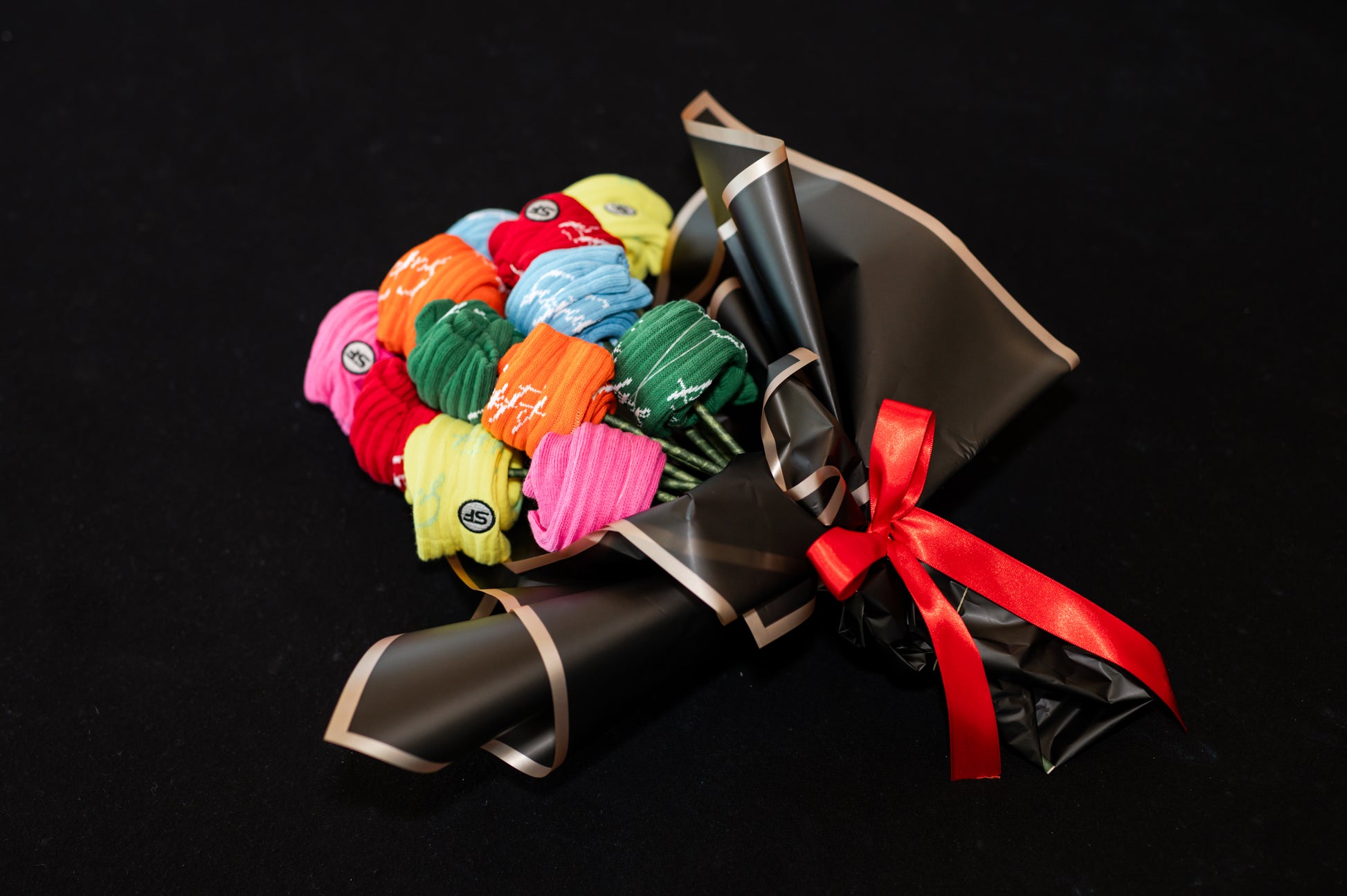 A bouquet of multicolored crew compression socks with a red ribbon, arranged in a manner resembling a traditional flower bouquet, on a black background.