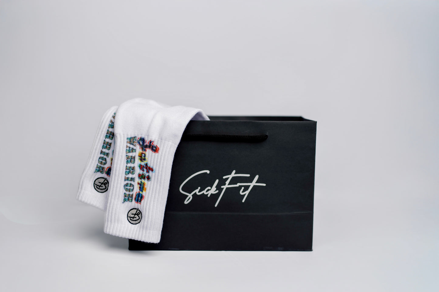 A pair of white crew compression socks that have the text "Latina Warrior" inside a black bag with the name "SickFit"