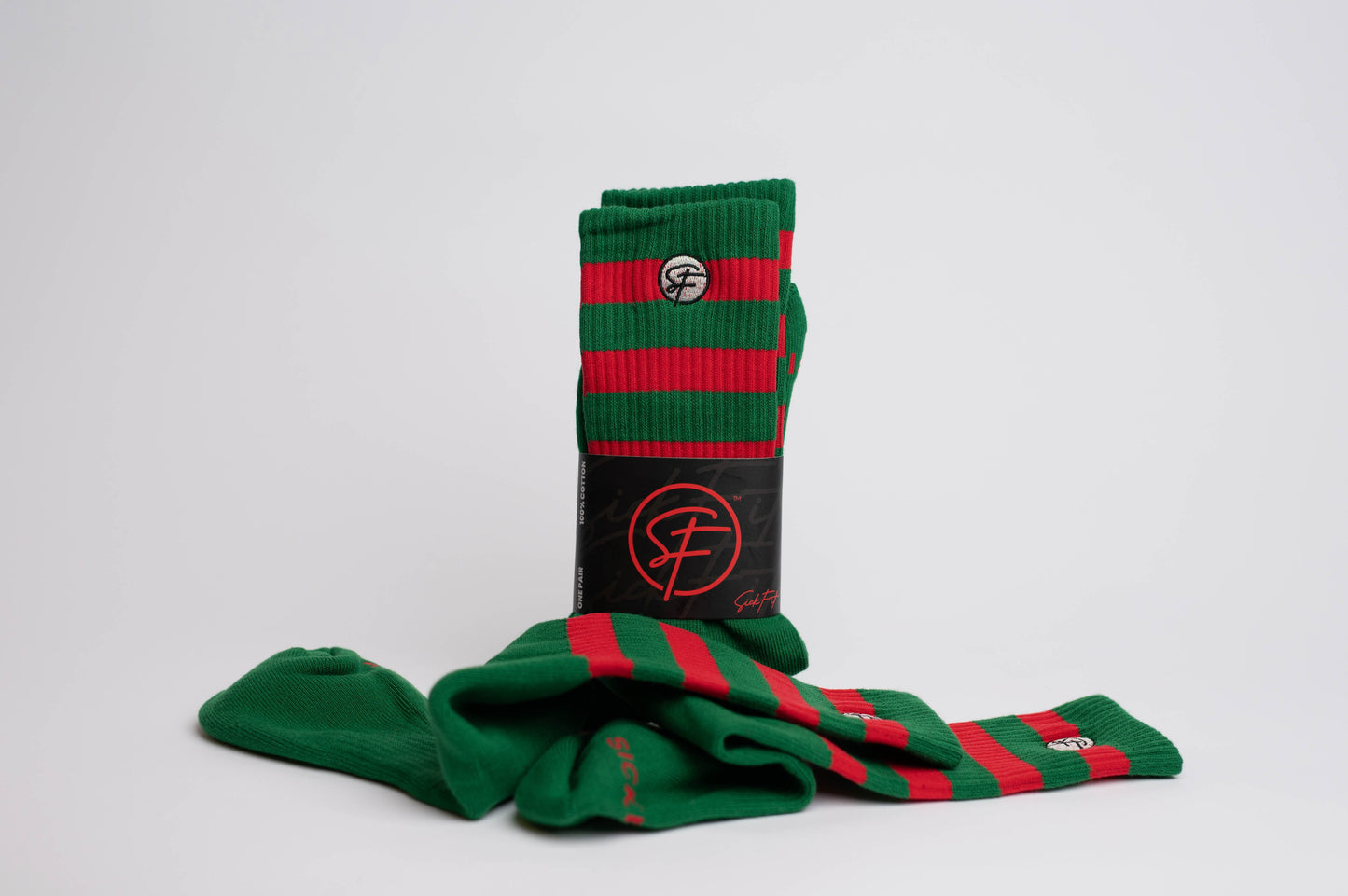 A pair of crew compression holiday socks with bold green and vibrant red stripes, placed on a white surface next to a black SickFit branded bag.