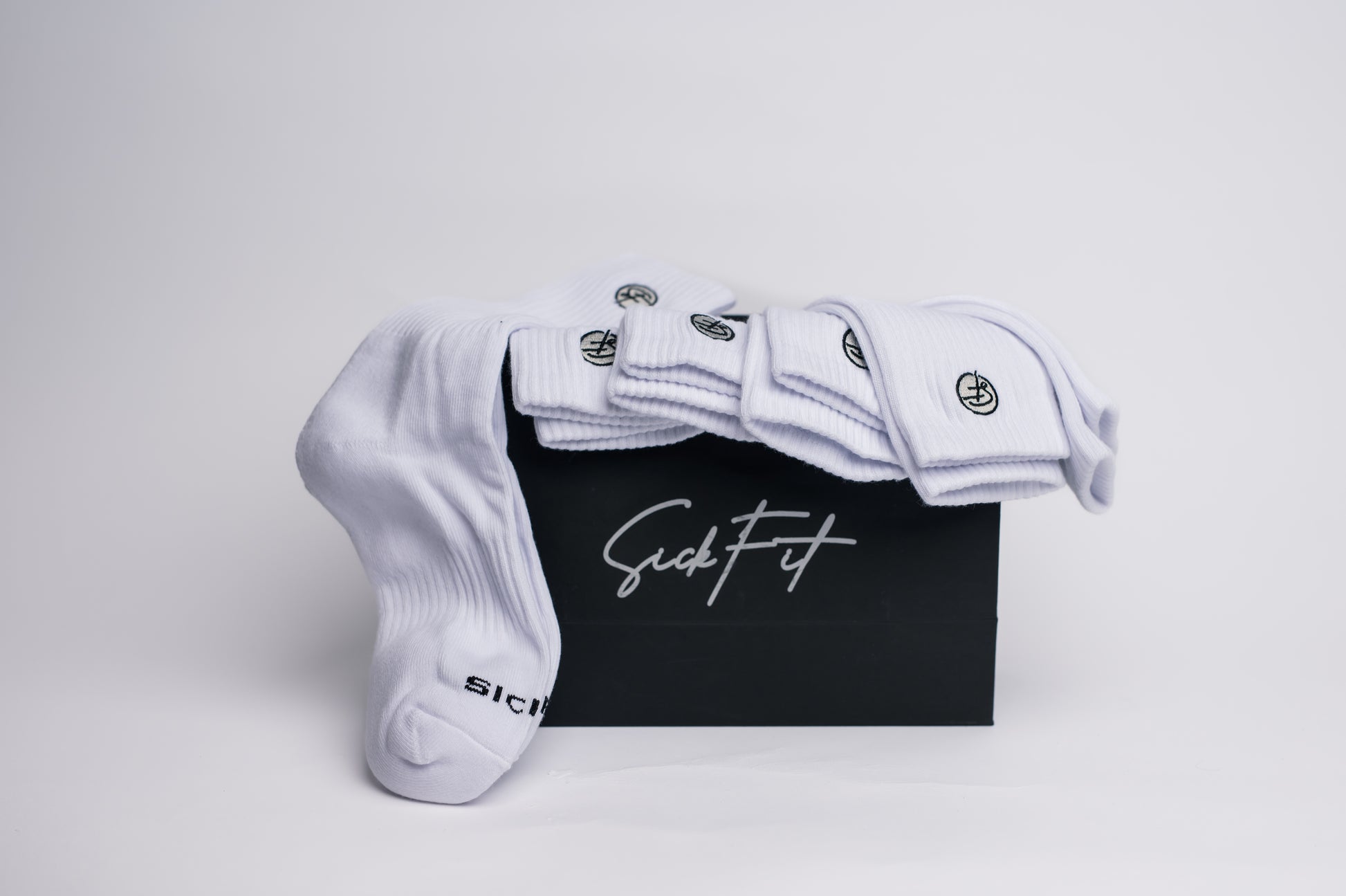 A pack of white crew compression  socks with black detailing, displayed alongside a black box with white text on it, presumably the product 'The Core 6 (6-Pack)' by SICKFIT.