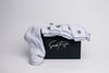 A pack of white crew compression  socks with black detailing, displayed alongside a black box with white text on it, presumably the product 'The Core 6 (6-Pack)' by SICKFIT.