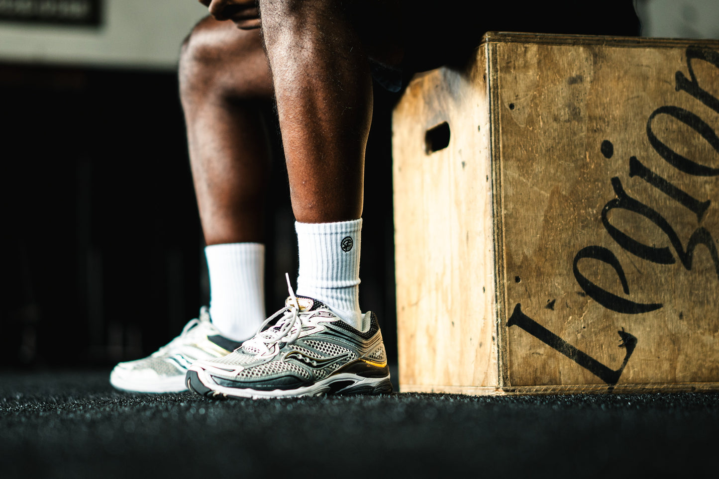 Person sitting on a wooden box with 'Legion' branding, wearing athletic shoes and white socks.