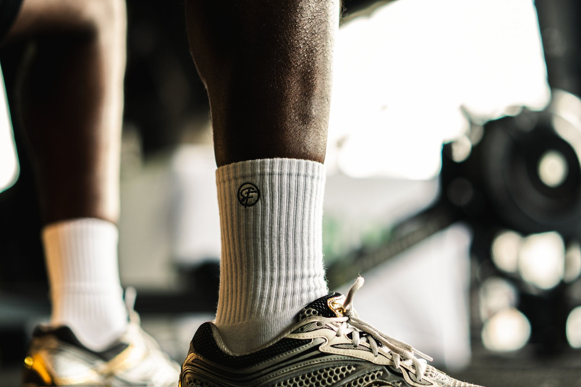 Person wearing white athletic socks with a SickFit logo and black athletic shoes on a blurred background