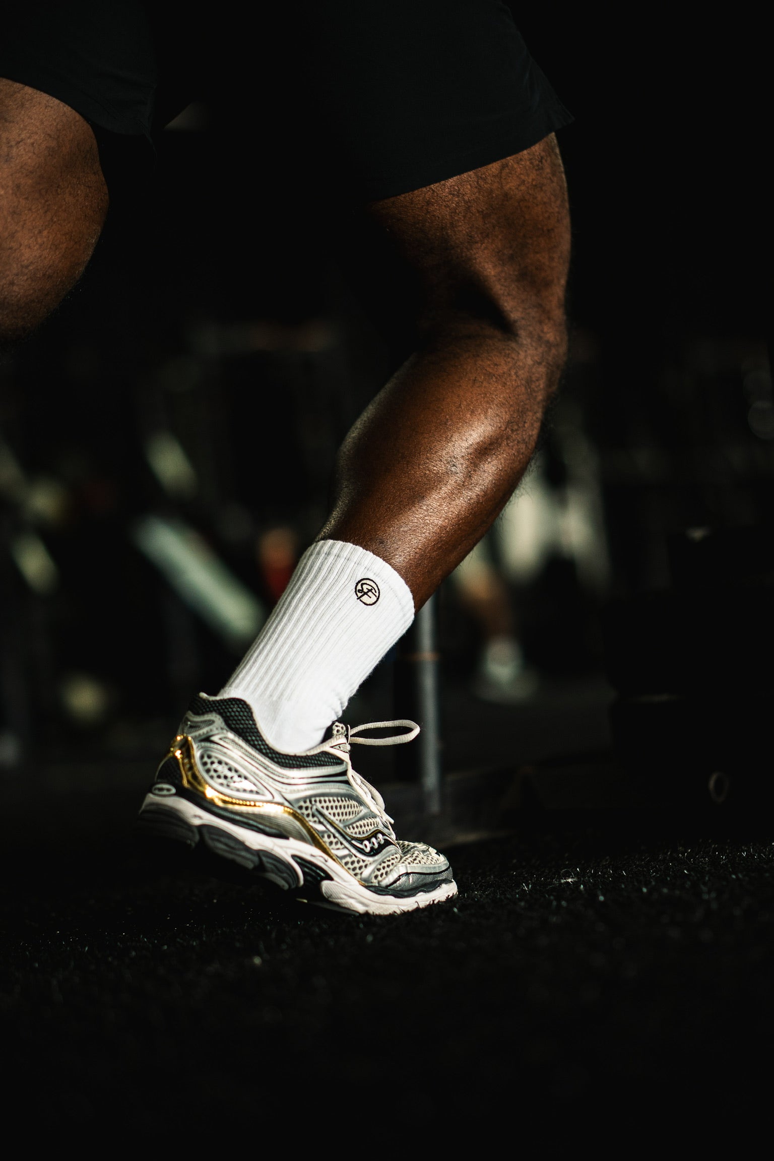 Person wearing a white crew athletic sock and grey athletic shoe on a dark back