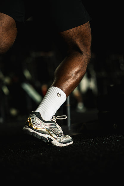 Person wearing a white crew athletic sock and grey athletic shoe on a dark back
