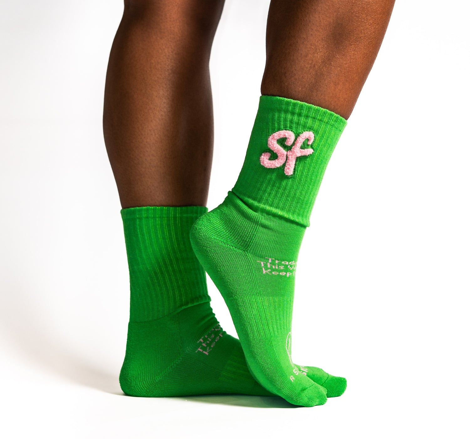Green crew athletic socks with pink lettering worn by a person on a white background