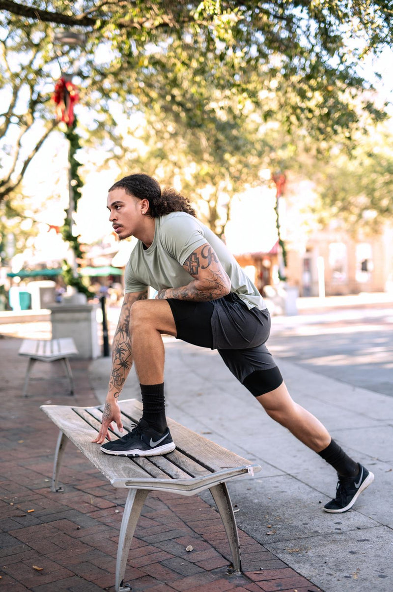 Man stretching on a bench outdoors with trees and buildings in the background