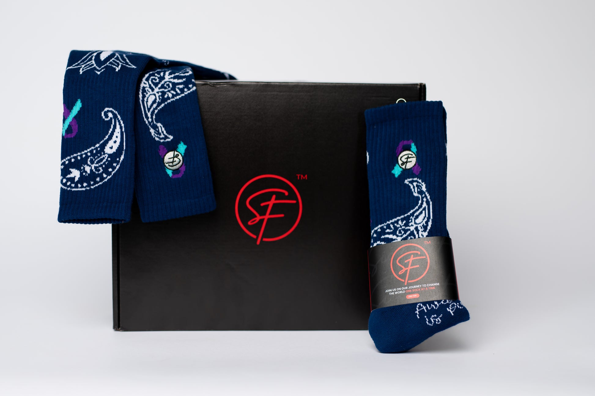 Two pairs of blue crew compression socks with colorful designs on a black box featuring a red logo.