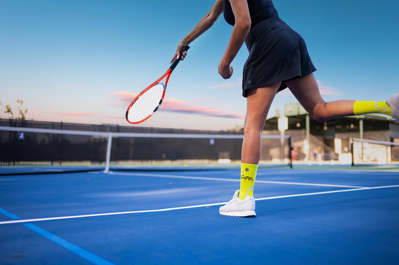 Person playing tennis on a court with a racket, wearing a skirt and tennis themed athletic socks.